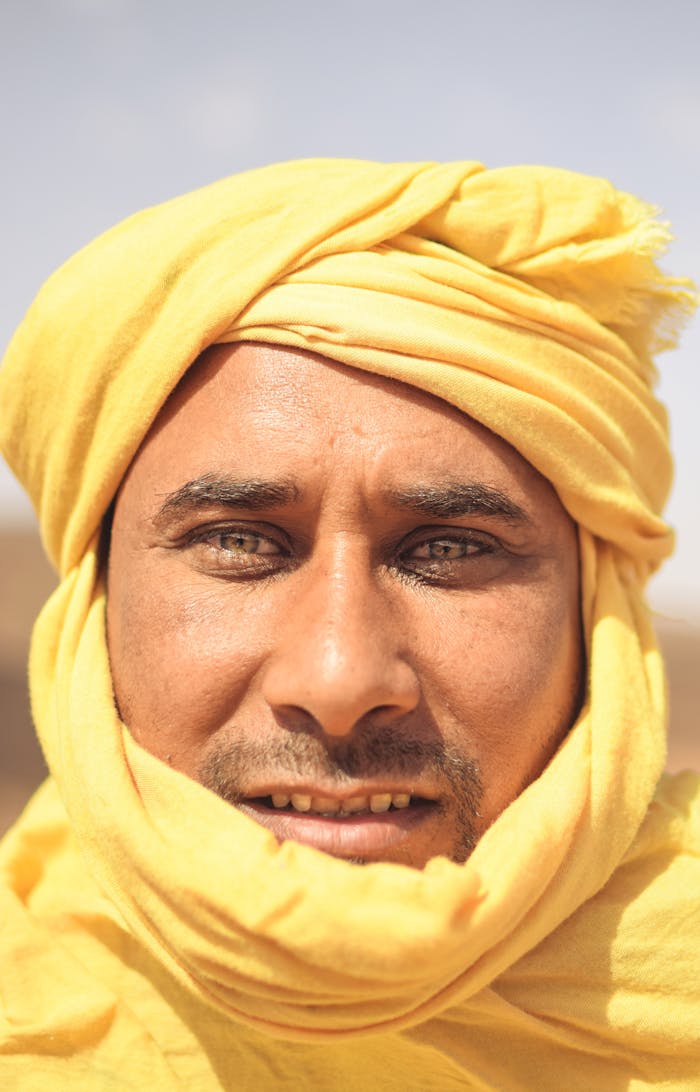 Close-up portrait of an Algerian man wearing a traditional yellow headscarf under the bright sun.